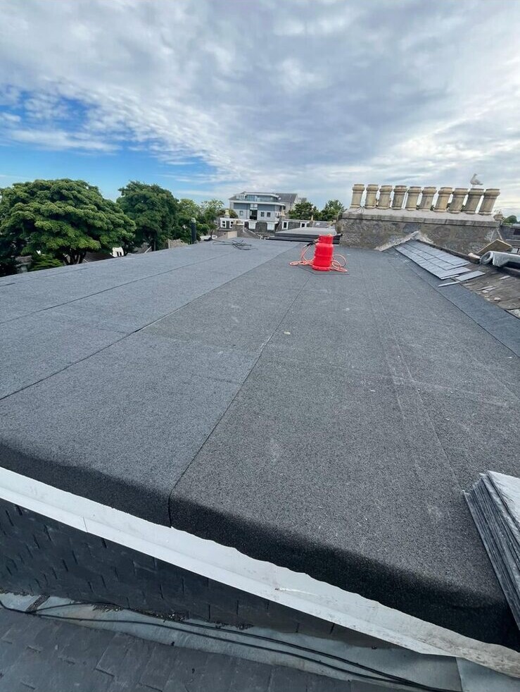 New grey mineral felt flat roof beside chimney pots
